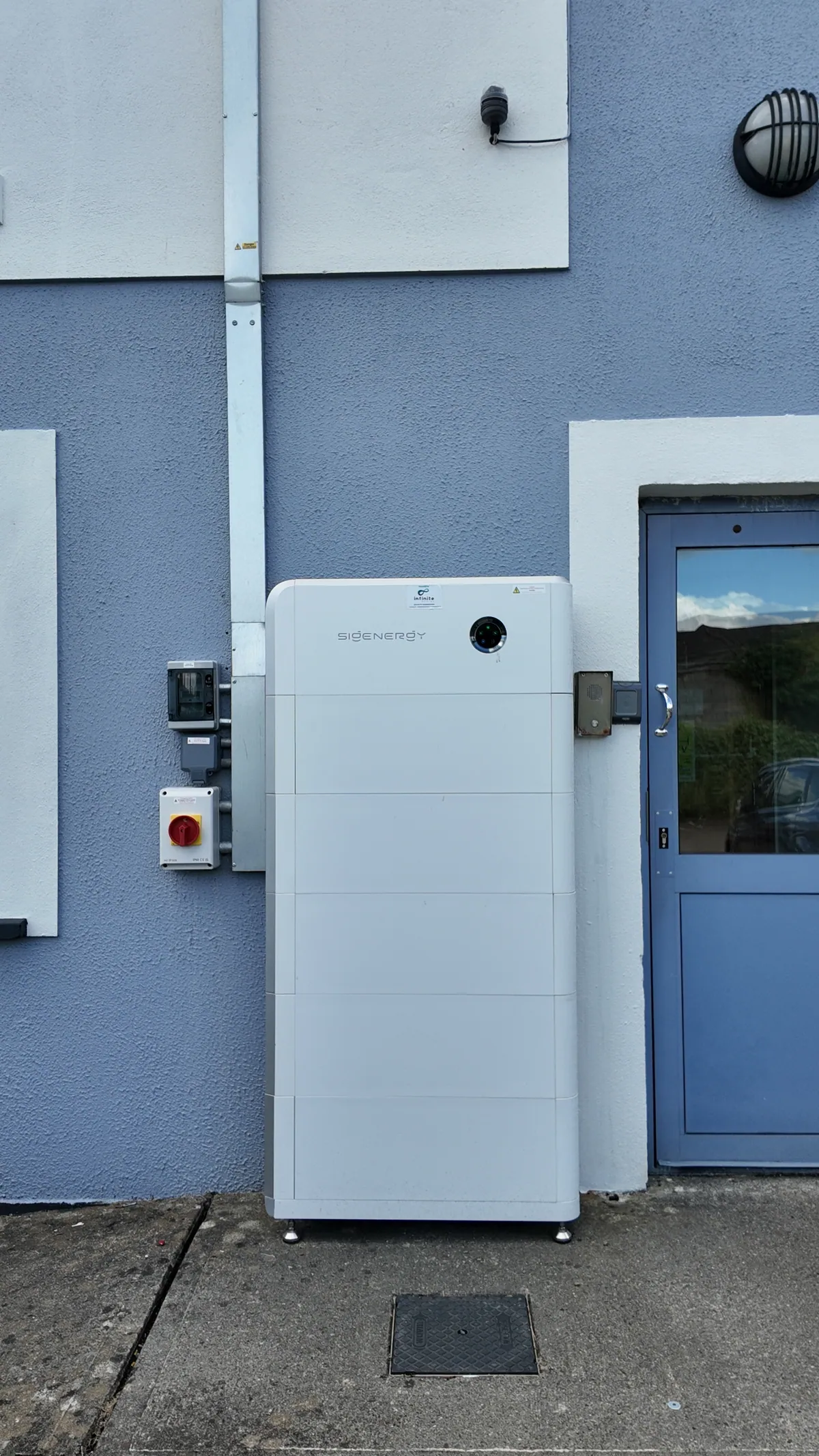 A Sigenergy storage unit and electrical equipment against a blue wall.