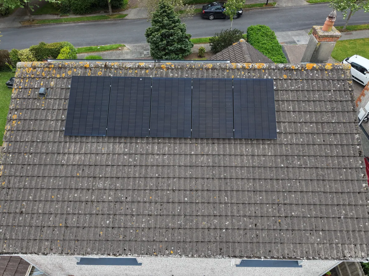 Five solar panels on the tiled roof of a home, viewed from above.