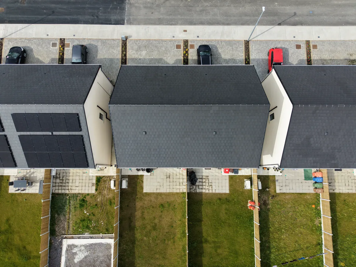Solar panels on one of three neighbouring house roofs, viewed from above.
