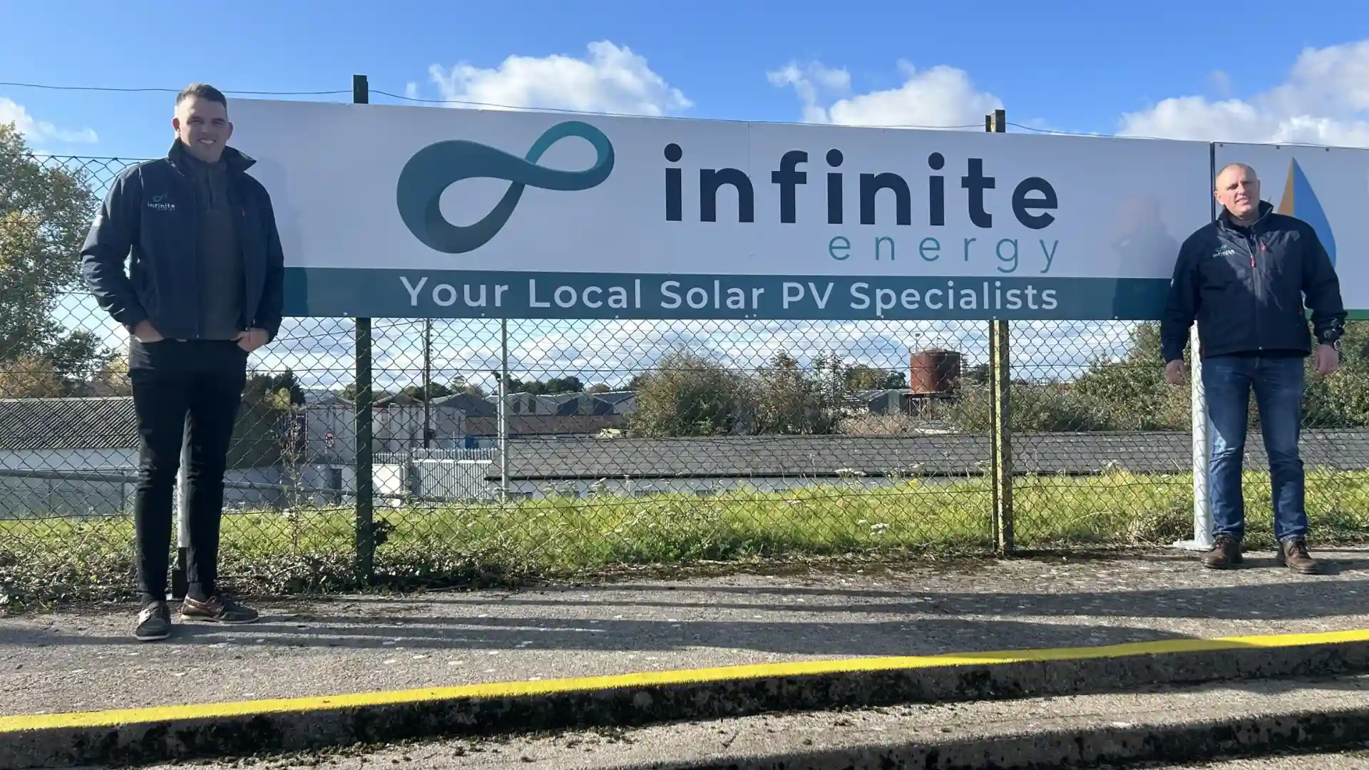 Two members of the Infinite Energy team beside the company sign.